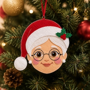 May include: A felt ornament shaped like a face with white hair, wearing a red and white Santa hat with a white pom-pom. The face features round black glasses, pink cheeks, and a small holly sprig with red berries attached to the hat brim.