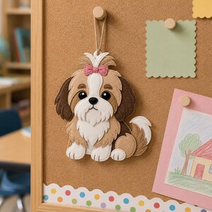 May include: A felt Shih Tzu dog ornament with brown, white, and tan fur, a pink bow, and black eyes. The dog is hanging on a corkboard with a drawing of a house and a green square note.