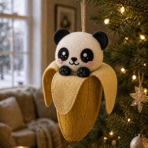 May include: A felt panda bear ornament with black ears, eyes, and paws, and pink cheeks, nestled in a yellow banana peel. The ornament hangs from a string, perfect for holiday decor.