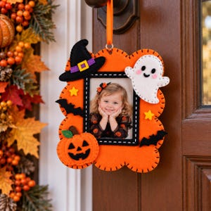 May include: A scalloped orange felt picture frame hanging by an orange ribbon. The frame features felt decorations including a black witch hat with a purple band, a white ghost, a jack-o'-lantern, two black bats, and two yellow stars.