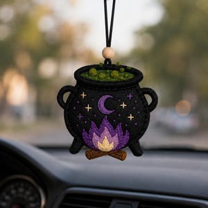 May include: A black felt hanging ornament shaped like a cauldron with green bubbling liquid, a purple crescent moon, yellow and purple stars, and a purple and yellow flame over brown logs, suspended by a black cord with a light wood bead.