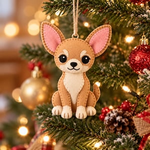 Puede incluir: Un adorno de fieltro con forma de chihuahua, de cuerpo color canela, pecho y patas color crema, y grandes orejas con forro rosa. El perro tiene ojos negros, nariz negra y boca bordada. Está colgado de un cordel de yute con costuras visibles.