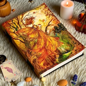 May include: A decorative journal with a detailed illustration of a woman in a flowing gown, set against a backdrop of trees and a full moon. The cover features a metal clasp. The journal is surrounded by candles, crystals, and star-shaped decorations.