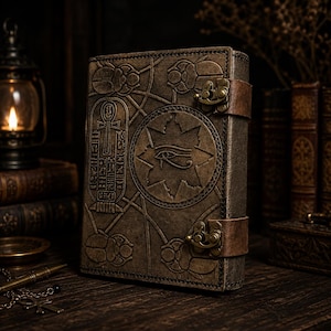 May include: A brown leather journal featuring embossed Egyptian symbols, including hieroglyphs, scarabs, and the Eye of Horus. It has a leather strap closure and brass fittings. The dark brown cover has a textured finish, giving it an antique or vintage aesthetic.