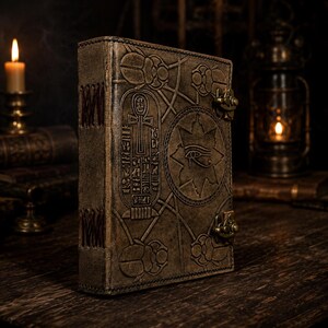 May include: A brown leather journal featuring embossed Egyptian symbols, such as an ankh, eye of Horus, and scarab beetles. The journal has a clasp closure and a stitched spine, creating an ancient look.