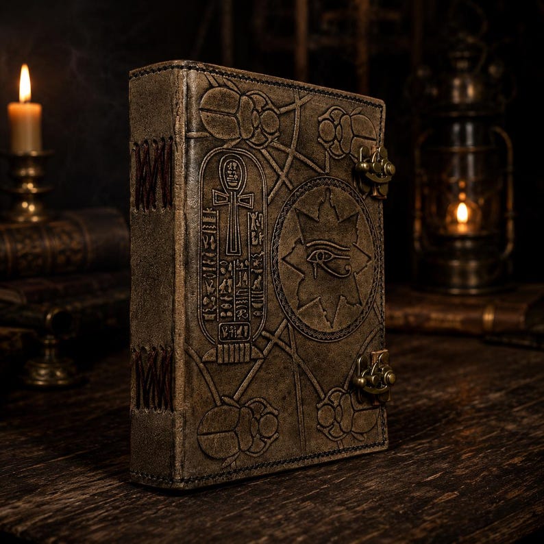 May include: A brown leather journal featuring embossed Egyptian symbols, such as an ankh, eye of Horus, and scarab beetles. The journal has a clasp closure and a stitched spine, creating an ancient look.