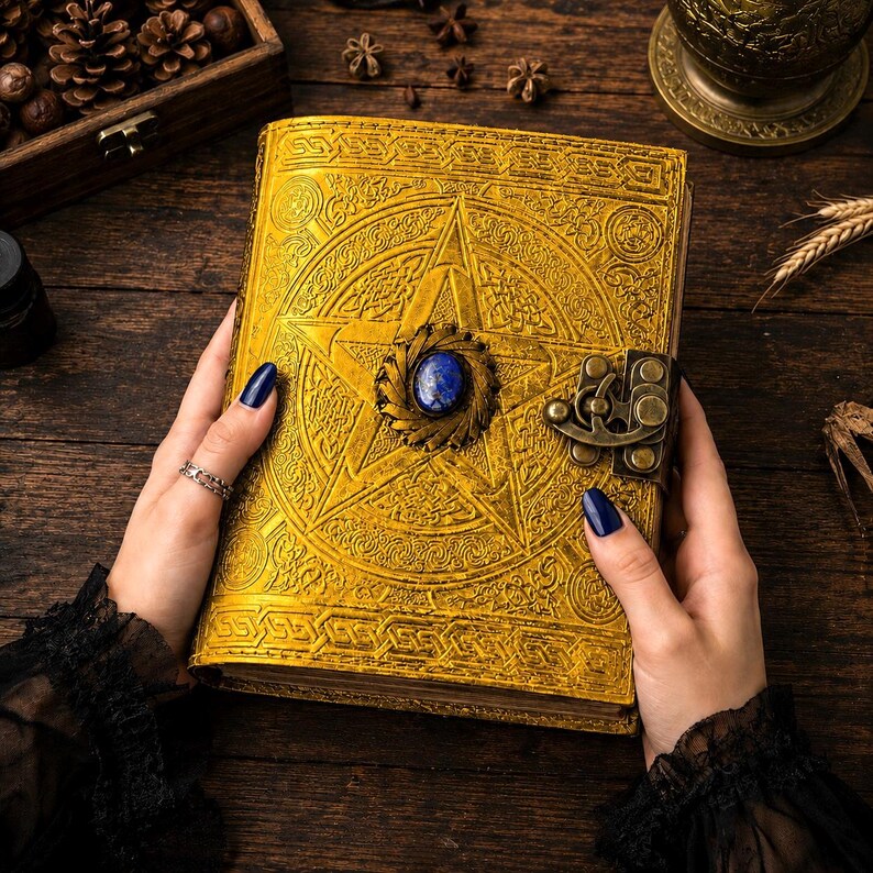 Peut inclure: Un journal en cuir jaune dor&eacute; avec un pentagramme en relief et une pierre pr&eacute;cieuse bleue au centre. Le journal a un fermoir orn&eacute; et est tenu par des mains avec du vernis &agrave; ongles bleu fonc&eacute;. La couverture est tr&egrave;s d&eacute;taill&eacute;e.
