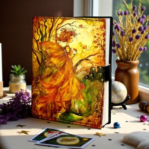 May include: A leather-bound journal with a fantasy art cover. The cover features a woman in a flowing orange dress with a large moon in the background. The journal has a black spine and a metal clasp.
