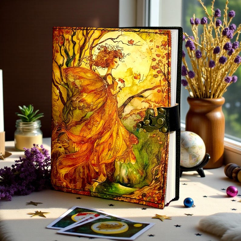 May include: A leather-bound journal with a fantasy art cover. The cover features a woman in a flowing orange dress with a large moon in the background. The journal has a black spine and a metal clasp.
