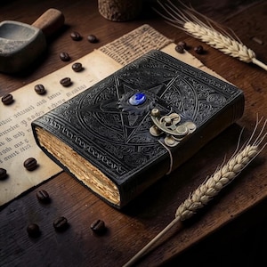 Peut inclure: Un journal en cuir noir avec un pentagramme en relief et une pierre pr&eacute;cieuse bleue. Le journal a un fermoir en m&eacute;tal et des pages dor&eacute;es vieilles. Des grains de caf&eacute; et des &eacute;pis de bl&eacute; sont dispers&eacute;s sur une surface en bois.