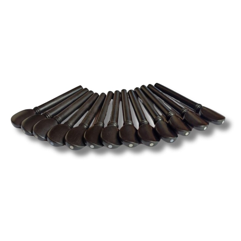 May include: A collection of dark brown violin pegs arranged in a semi-circle. Each peg has a rounded head with a small, white dot and a long, tapered shaft. The pegs are made of wood and appear to be new.