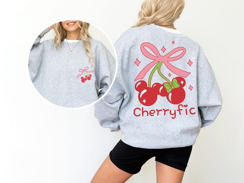 May include: A light gray crewneck sweatshirt featuring a large graphic on the back of two red cherries shaped like mouse ears, tied with a pink bow and accented with sparkles. The word Cherryfic is printed below in red. A smaller version is on the front.