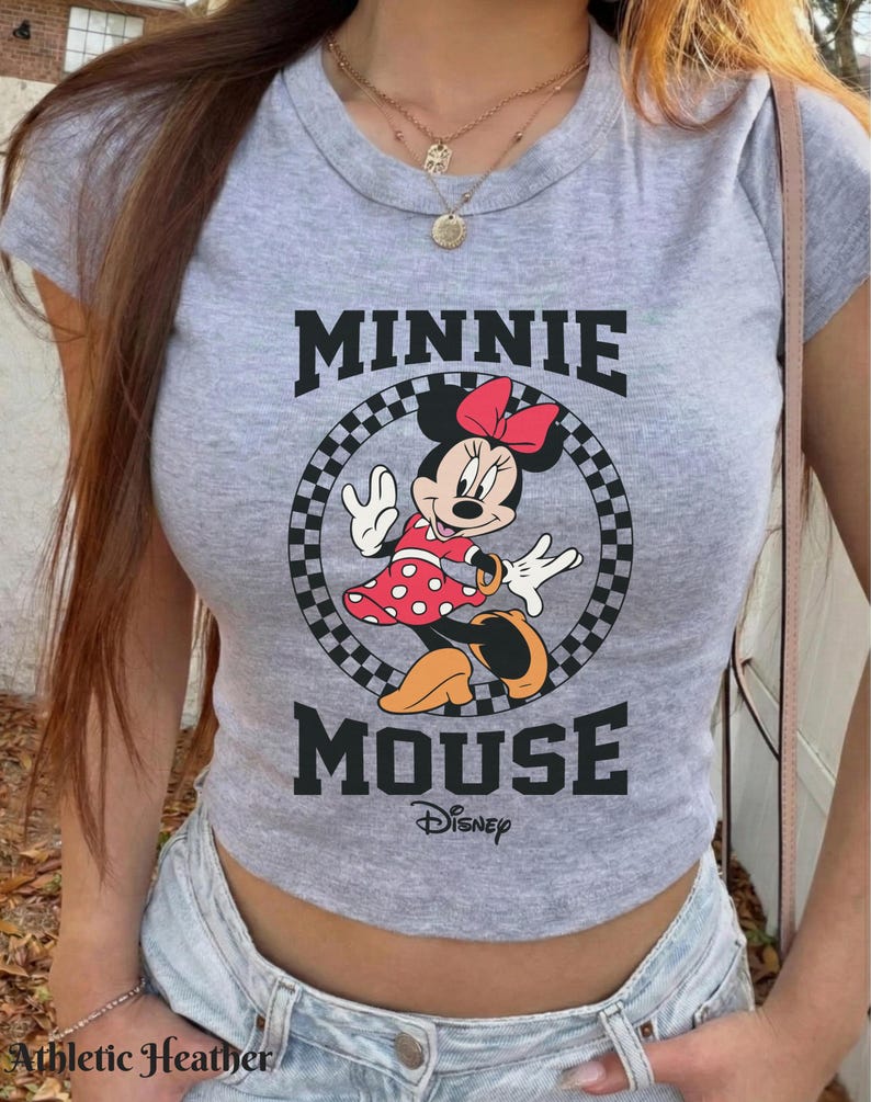 K&ouml;nnte beinhalten: Graues Crop-Top mit Minnie Mouse-Grafik. Das Design zeigt die Worte "MINNIE MOUSE" in schwarzen Buchstaben, mit Minnie Mouse in einem roten Polka-Dot-Kleid und einer roten Schleife. Das Disney-Logo befindet sich darunter.