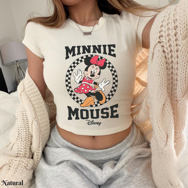 K&ouml;nnte beinhalten: Cremefarbenes Crop-Top mit Minnie Mouse-Grafik. Das Design enth&auml;lt die schwarzen W&ouml;rter "MINNIE MOUSE", mit Minnie in einem roten gepunkteten Kleid. Das Top hat einen runden Ausschnitt und kurze &Auml;rmel.