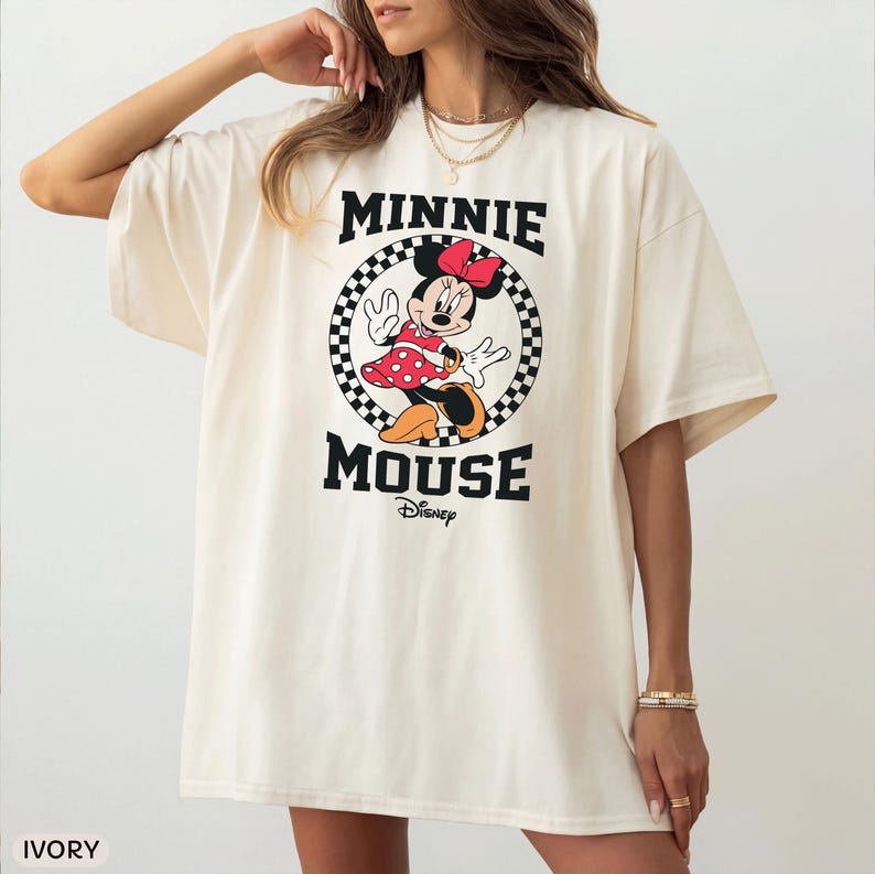 May include: Ivory-colored oversized t-shirt featuring a Minnie Mouse graphic. The graphic includes Minnie in a red polka-dot dress, a red bow, and the words "MINNIE MOUSE" in black, with "Disney" below. The shirt has short sleeves.