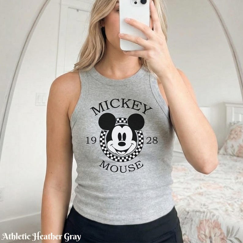 Op de afbeelding: Athletic heather grijze tanktop met een zwart-wit Mickey Mouse-afbeelding. De afbeelding bevat de tekst "MICKEY MOUSE" en de cijfers "1928". De tanktop is een geribde knit.