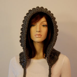 May include: A gray, handmade crochet hood with a textured, scalloped edge. The hood features two buttons and long ties. The hood is designed to be worn over the head and shoulders.