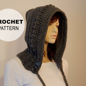 Peut inclure: Un capuchon crocheté gris foncé avec des rabats d'oreille et deux gros boutons. Le capuchon est présenté sur un mannequin. Le texte "CROCHET PATTERN" est dans un cercle blanc en haut à gauche.