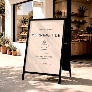 Puede incluir: Un letrero de acera en forma de A de color negro con un tablero blanco que presenta el texto "ARTISAN ROAST MORNING TIDE SMALL BATCH ROASTED IN OCEANSIDE EST. 2021" y un icono de línea de una taza de café humeante centrado.