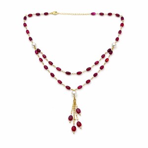 May include: A double-strand necklace featuring small, oval-shaped deep red beads and white pearls interspersed along a thin gold-tone chain. The center of the necklace displays a dangling tassel element composed of gold chains and red beads.
