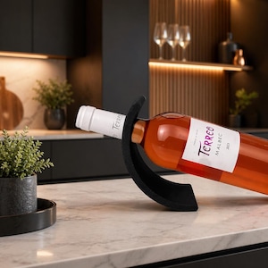 Peut inclure: Une bouteille de vin Terreo Malbec 2021 dans un support à vin noir. La bouteille est inclinée, montrant son étiquette et le vin rosé. Le support est sur un comptoir en marbre dans une cuisine.