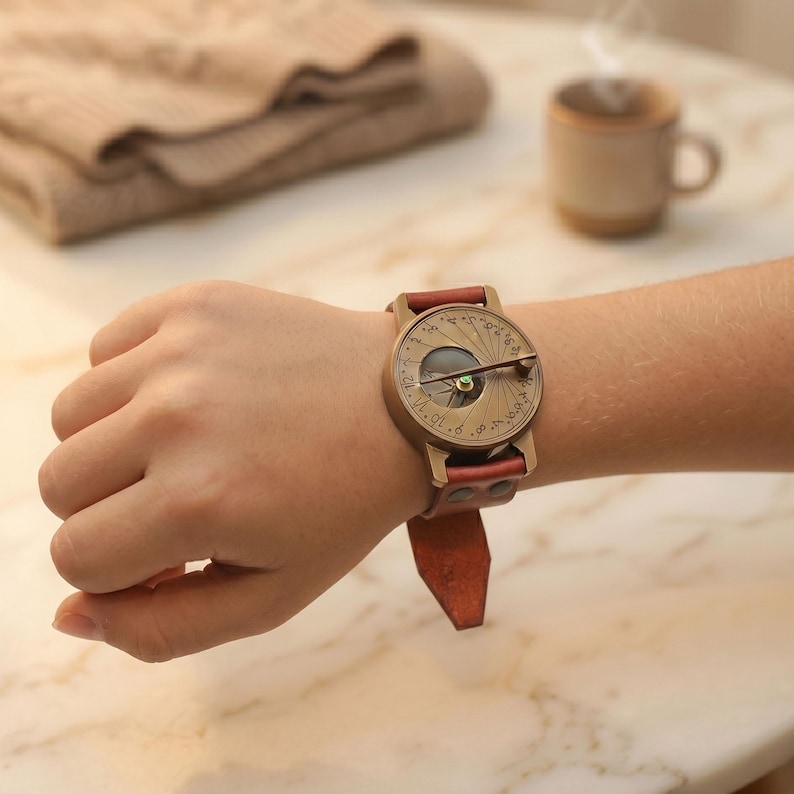 May include: A sundial wristwatch featuring a circular bronze-toned face with engraved numerical markings and a central gnomon. The timepiece is secured with a reddish-brown leather strap that includes visible metal rivets near the watch casing.