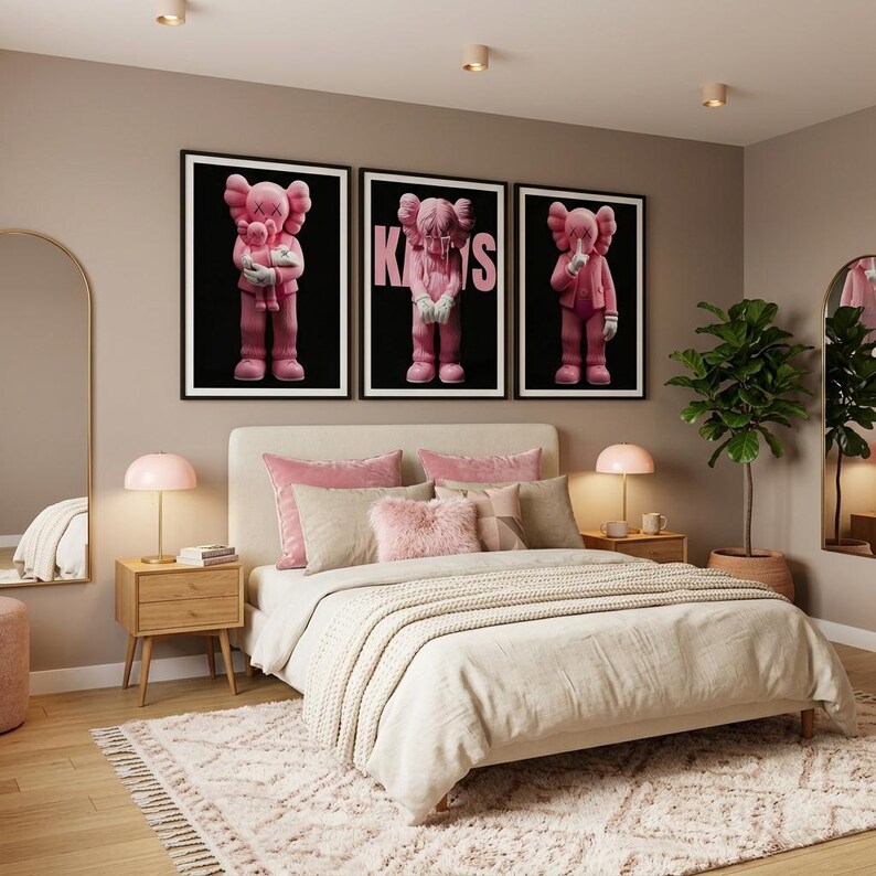 Pu&ograve; includere: Una scena di camera da letto con un letto con lenzuola rosa e beige, un tappeto fantasia e tre opere d'arte incorniciate con figure rosa su sfondo nero. Due lampade rosa sono sui comodini in legno. Uno specchio e una pianta in vaso completano l'arredamento.