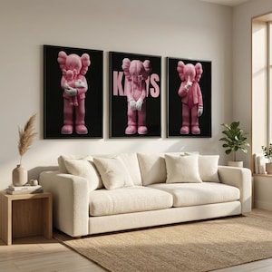 Pu&ograve; includere: Tre stampe artistiche incorniciate con personaggi rosa dei cartoni animati su sfondo nero. I personaggi hanno occhi a forma di X e sono in varie pose. Le stampe sono appese sopra un divano color crema in un salotto moderno.