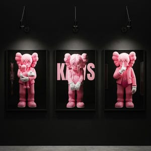 Pu&ograve; includere: Tre opere d'arte KAWS rosa incorniciate su un muro nero. Ognuna presenta una diversa figura KAWS. Una tiene una figura pi&ugrave; piccola, un'altra ha la parola "KAWS" in rosa e la terza ha un dito sulle labbra.