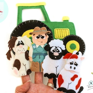 Op de afbeelding: Vilt vingerpoppen van een boer, een hond, een schaap en een koe. De poppen staan voor een groene vilt tractor met gele wielen.