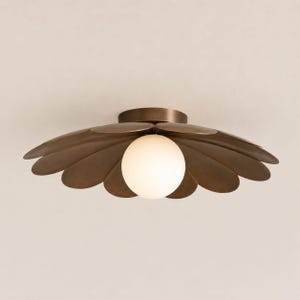 Può includere: Un lampadario da soffitto color bronzo con un design floreale. L'apparecchio ha una lampadina bianca sferica centrale, circondata da elementi a forma di petalo. La luce è montata su un soffitto bianco.