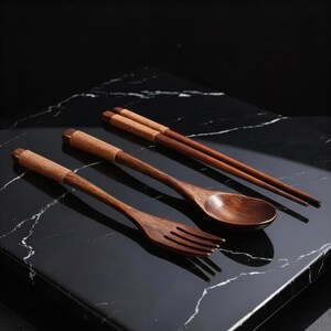 May include: A wooden dining set featuring a fork, spoon, and chopsticks. The utensils are made of dark brown wood with woven accents on the handles. The set is displayed on a black marble surface.