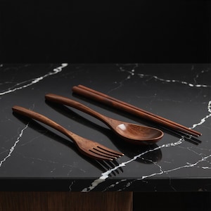 May include: A wooden fork, spoon, and chopsticks set. The utensils are made of a dark brown wood and are arranged on a black marble surface. The fork has three tines, and the spoon has a rounded bowl.