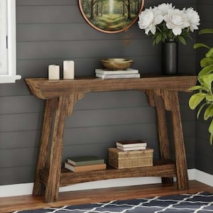 Puede incluir: Una consola rústica de madera con una balda inferior. La mesa es de madera envejecida con un acabado natural. Está decorada con velas, libros, un cuenco decorativo y un jarrón con flores blancas. La mesa mide unos 152 cm de largo.