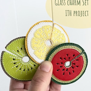 Könnte beinhalten: Ein Set aus drei fruchtförmigen Glasanhängern: eine Kiwi, eine Zitrone und eine Wassermelone. Jeder Anhänger besteht aus genähtem, lederähnlichem Material mit detaillierten Nähten und einem Loch zum Aufhängen. Der Text "GLASS CHARM SET ITH PROJECT" ist sichtbar.