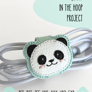 Op de afbeelding: Een mintgroene kabelorganizer met een geborduurd pandagezicht van wit gestructureerd materiaal, zwarte oren en roze wangen. De tekst luidt QUICK IN THE HOOP PROJECT en vermeldt de bestandsformaten .PES .DST .JEF .HUS .XXX .VP3 .EXP.