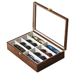 May include: A rectangular wooden storage box with a hinged glass lid and a gold-toned metal latch. The interior is lined with light beige fabric and divided into six individual compartments, each containing a pair of sunglasses with various frames.