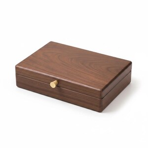 May include: A rectangular wooden box with a dark brown wood grain finish and a smooth surface. The box features a hinged lid and a small, circular, metallic gold-colored knob centered on the front edge for opening and closing the container.