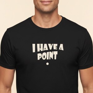 Puede incluir: Una camiseta negra de manga corta con el texto blanco "I HAVE A POINT" impreso en el pecho en una fuente negrita sin remates, con un pequeño punto circular blanco situado justo debajo de la palabra "POINT" en la parte delantera.