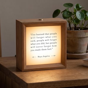 Könnte beinhalten: Eine quadratische Lichtbox aus Holz mit einer warm beleuchteten Frontplatte, auf der das Zitat aufgedruckt ist: "I've learned that people will forget what you said, people will forget what you did, but people will never forget how you made them feel." - Maya Angelou.