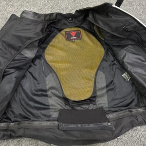 K&ouml;nnte beinhalten: Schwarze Motorradjacke mit gelbem R&uuml;ckenprotektor und Mesh-Futter. Die Jacke hat einen Rei&szlig;verschluss und mehrere Taschen. Das Innere zeigt ein rot-wei&szlig;es Logo.