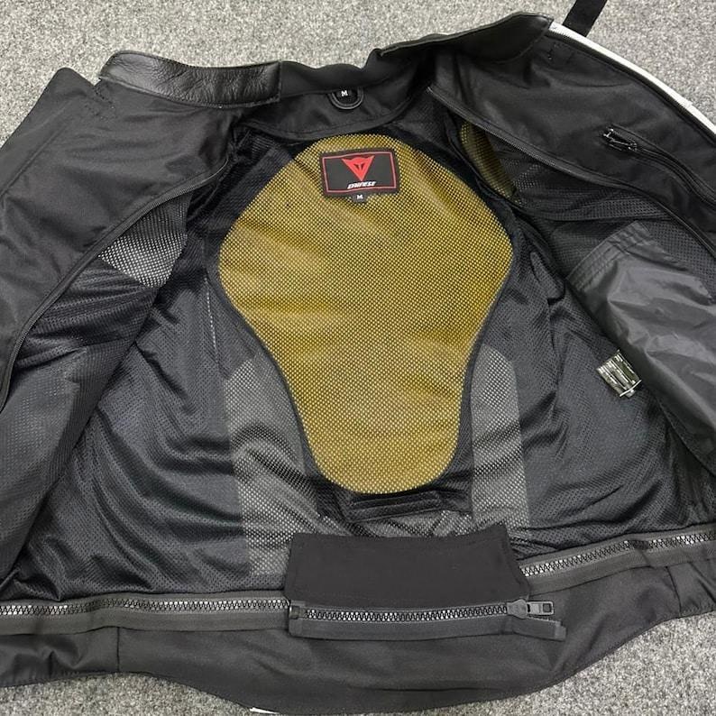 K&ouml;nnte beinhalten: Schwarze Motorradjacke mit gelbem R&uuml;ckenprotektor und Mesh-Futter. Die Jacke hat einen Rei&szlig;verschluss und mehrere Taschen. Das Innere zeigt ein rot-wei&szlig;es Logo.