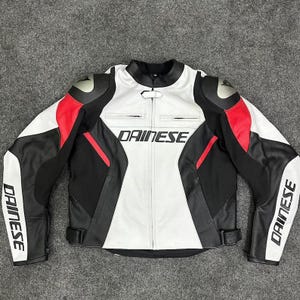 K&ouml;nnte beinhalten: Schwarze, wei&szlig;e und rote Motorradjacke aus Leder mit dem Markennamen "DAINESE" auf Brust und &Auml;rmeln. Die Jacke hat einen Stehkragen, Schulterpolster und einen Tailleng&uuml;rtel. Die Jacke ist auf Schutz und Stil ausgelegt.