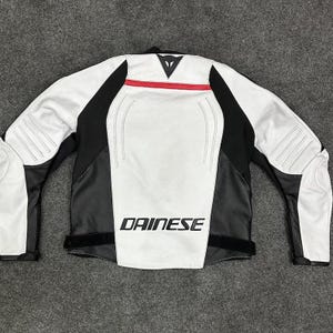 K&ouml;nnte beinhalten: Wei&szlig;-schwarze Motorradjacke mit roten Akzenten. Das "DAINESE"-Logo ist in wei&szlig;en Buchstaben auf der Vorderseite zu sehen. Die Jacke hat schwarze Eins&auml;tze an den Seiten und &Auml;rmeln sowie wei&szlig;e Eins&auml;tze auf der Vorder- und R&uuml;ckseite.