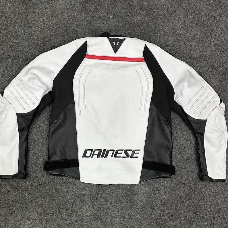 K&ouml;nnte beinhalten: Wei&szlig;-schwarze Motorradjacke mit roten Akzenten. Das "DAINESE"-Logo ist in wei&szlig;en Buchstaben auf der Vorderseite zu sehen. Die Jacke hat schwarze Eins&auml;tze an den Seiten und &Auml;rmeln sowie wei&szlig;e Eins&auml;tze auf der Vorder- und R&uuml;ckseite.
