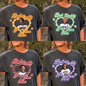 May include: Four dark gray t-shirts with different colored text and graphics. Each shirt has the words "But Daddy I Love Him" with a heart and a picture of a person. The text and heart colors are orange, green, red, and purple.