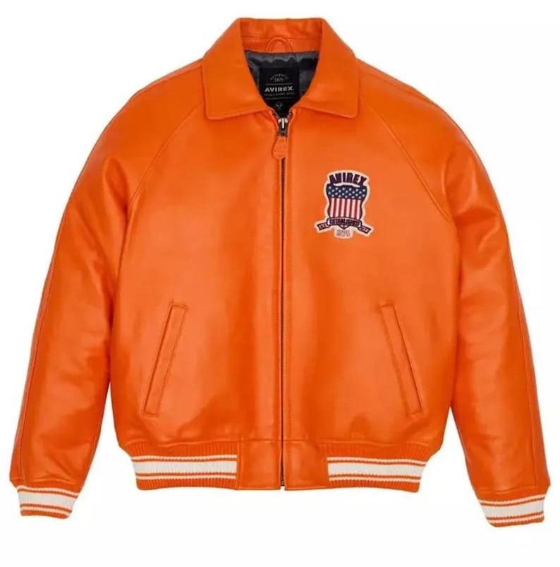 May include: Vibrant orange leather jacket with a zip closure, a collar, and a chest patch. The jacket features white and orange striped cuffs and hem. The patch displays a shield design with stars and stripes.