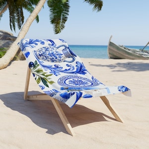 May include: A beach chair with a wooden frame and a fabric seat featuring a white and blue pattern of ornate ceramic vases, intricate floral scrolls, geometric Greek key borders, and small green olive branches with dark blue olives.