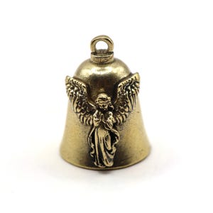 Puede incluir: Una pequeña campana de latón de estilo antiguo con una figura de ángel y alas. La campana tiene un lazo en la parte superior para colgar y está diseñada con detalles intrincados. El ángel está en posición de oración.