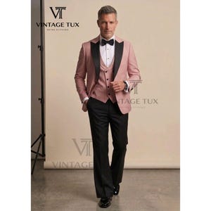 May include: A three-piece suit in a dusty rose color with black lapels and trousers. The suit includes a jacket, vest, and pants. A black bow tie and white dress shirt complete the formal ensemble. The brand name "VINTAGE TUX" is visible.
